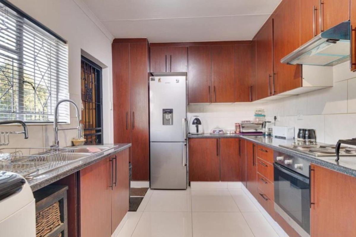 A functional kitchen featuring dark wood cabinetry, granite countertops, built-in oven, hob, extractor fan, and tiled flooring with a window overlooking the exterior.