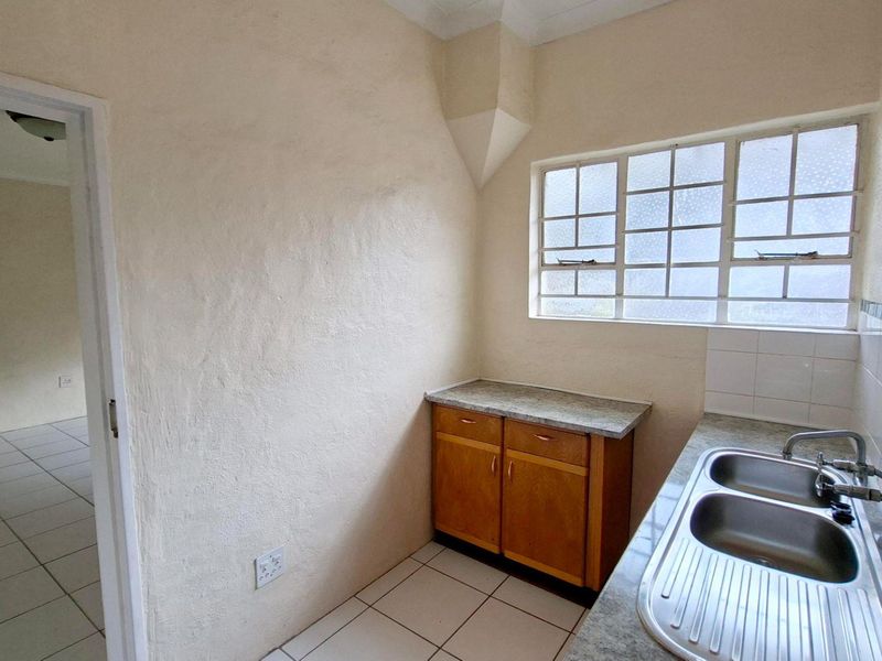 A compact scullery area featuring a double bowl stainless steel sink, laminate countertops, and built-in wooden cabinetry with tiled flooring.