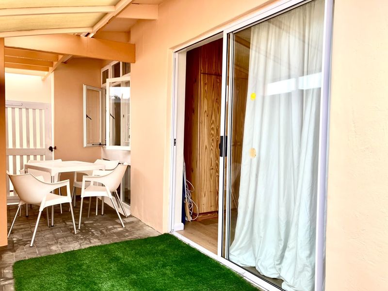 A covered patio area featuring paved flooring, artificial turf, and a sliding glass door providing access to the interior living space.