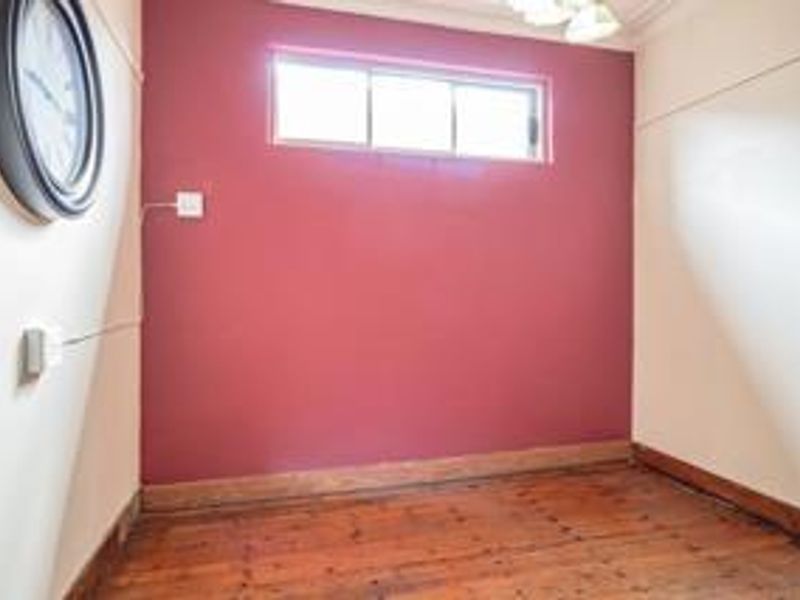 An empty bedroom featuring original timber flooring, a high-set clerestory window, and a bold accent wall, offering a blank canvas for interior design.