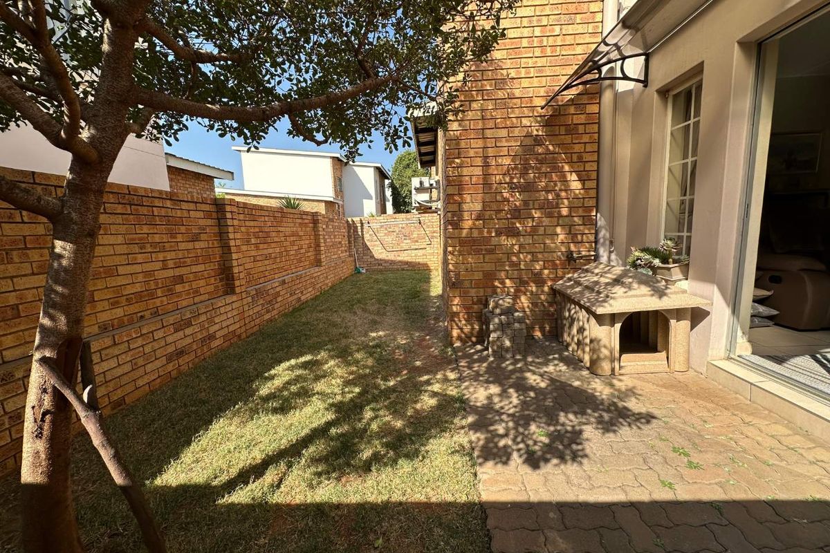 A private rear garden featuring a face brick boundary wall, paved patio area, and a small lawn accessible via a sliding door.