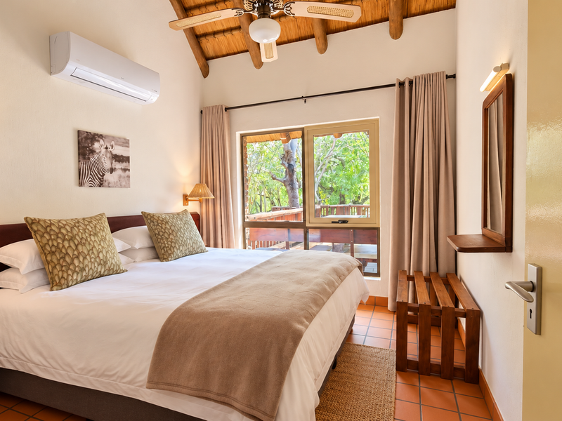 A well-maintained bedroom featuring exposed timber rafters, tiled flooring, air conditioning, and direct access to an outdoor patio area.