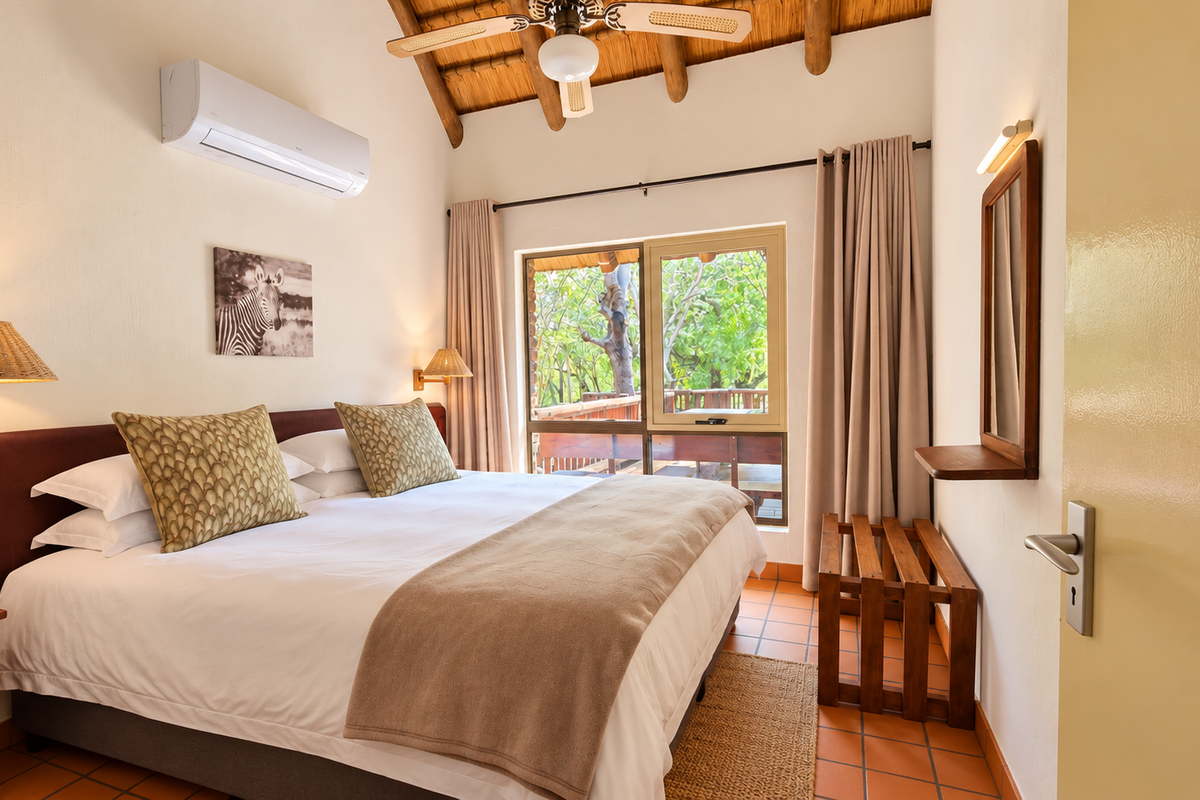 A well-maintained bedroom featuring exposed timber rafters, tiled flooring, air conditioning, and direct access to an outdoor patio area.