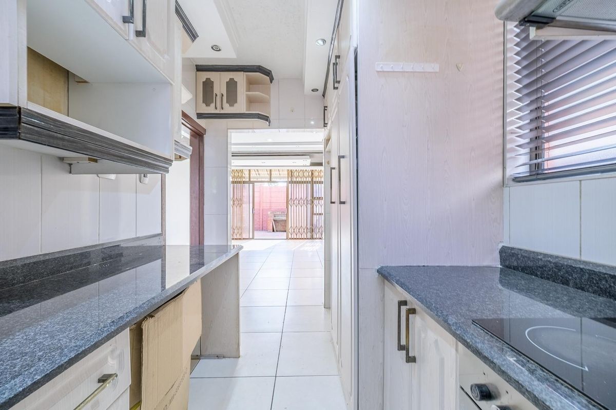 A galley-style kitchen featuring granite countertops, built-in cabinetry, and an electric hob, leading through to an open-plan living area.