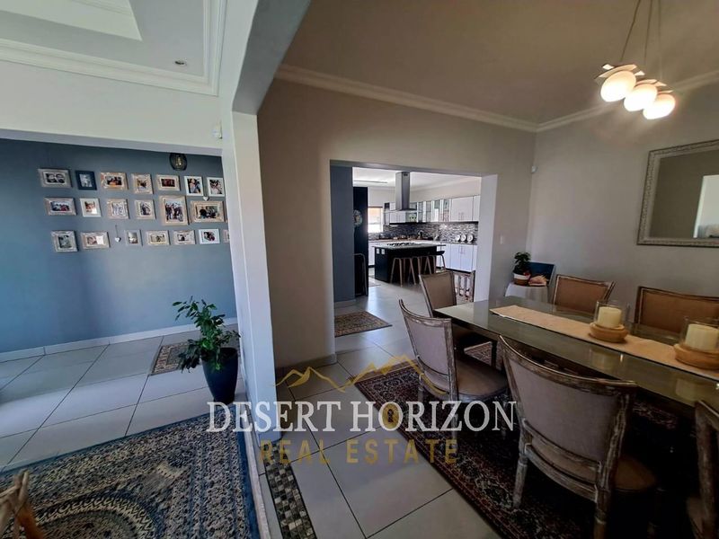 Open plan dining area flowing into a modern kitchen with a central island, tiled floors, and neutral wall finishes.