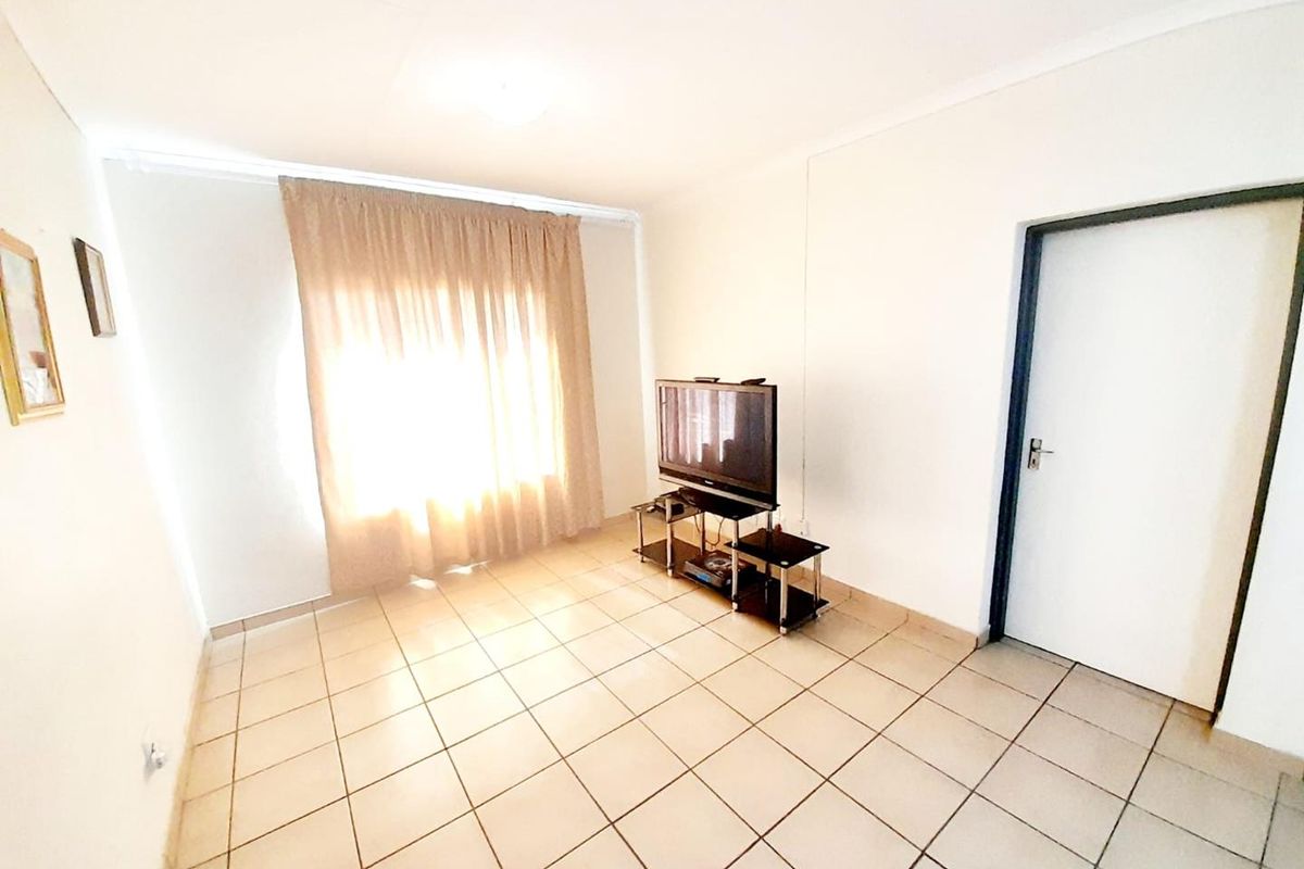 A simple living room featuring neutral tiled flooring and a single doorway, providing a clean and functional space.