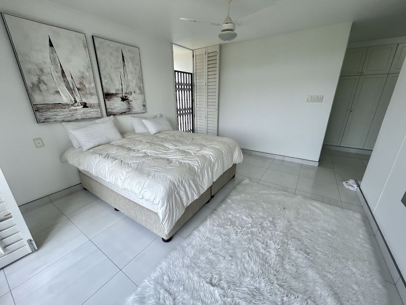 Spacious bedroom featuring neutral tiled flooring, built-in cupboards, a ceiling fan, and direct access to an outdoor area through a secure gate.