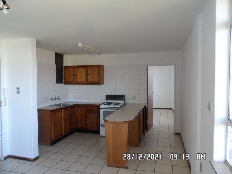 A dated kitchen featuring wooden cabinetry, a breakfast bar, and tiled flooring, offering a functional layout ready for modern renovation.