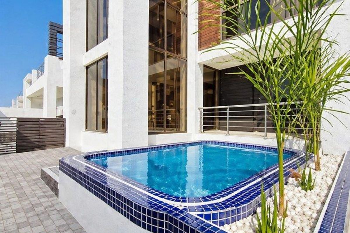 Modern multi-story residence featuring a sleek tiled plunge pool, stone-accented landscaping, and expansive glass windows overlooking a paved patio area.