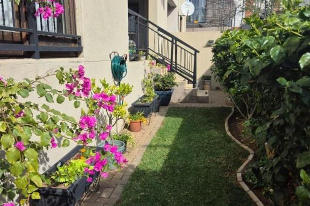 A well-maintained rear garden area featuring a paved walkway, a small lawn, and a metal staircase leading to the upper level of the apartment.