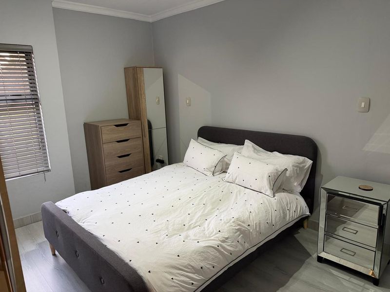 A well-maintained bedroom featuring neutral grey walls, laminate flooring, and venetian blinds, providing a clean and functional living space.