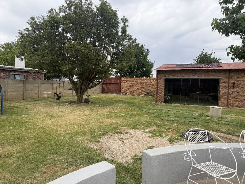 Spacious backyard featuring a large lawn, mature tree, and a detached facebrick outbuilding with sliding glass doors.