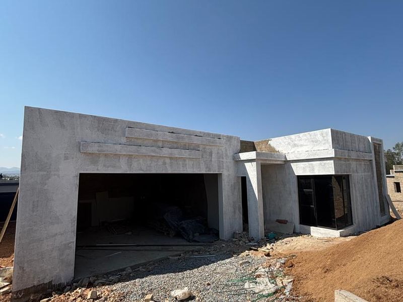 Front elevation of a modern house under construction, featuring a double garage, concrete facade, and aluminium window frames on an unlandscaped site.