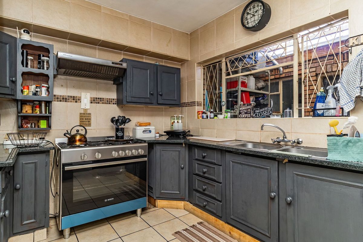 A functional kitchen featuring dark cabinetry, a gas stove with extractor fan, double sink, and tiled finishes throughout.