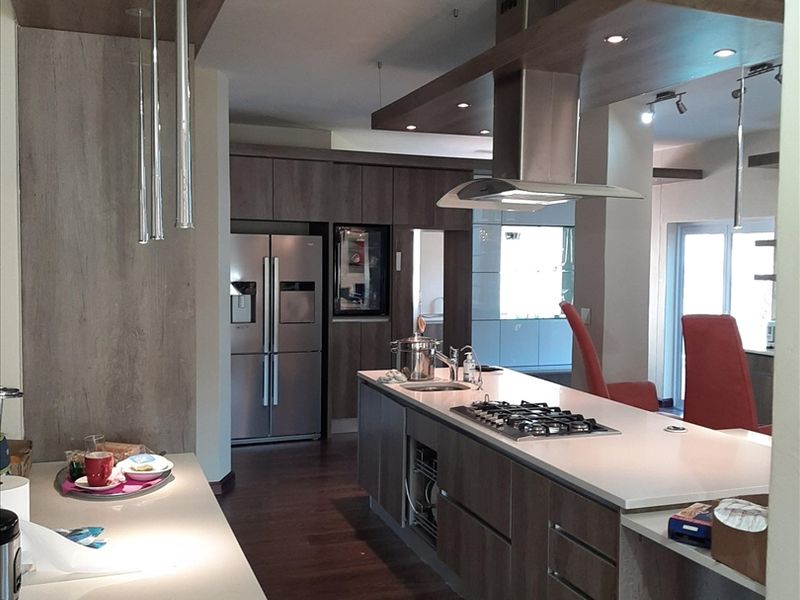 Modern kitchen featuring a large island with stone countertops, built-in gas cooktop, stainless steel extractor fan, and high-quality cabinetry with recessed and pendant lighting.
