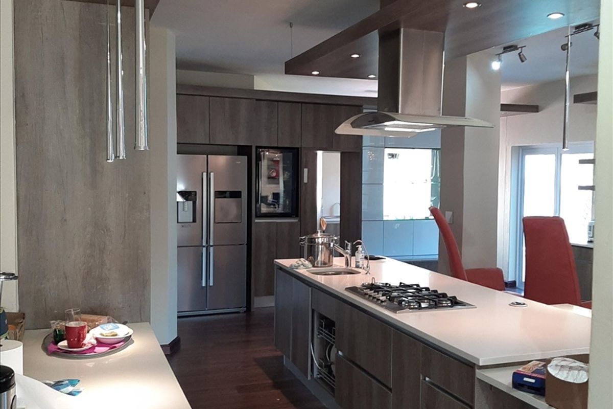 Modern kitchen featuring a large island with stone countertops, built-in gas cooktop, stainless steel extractor fan, and high-quality cabinetry with recessed and pendant lighting.