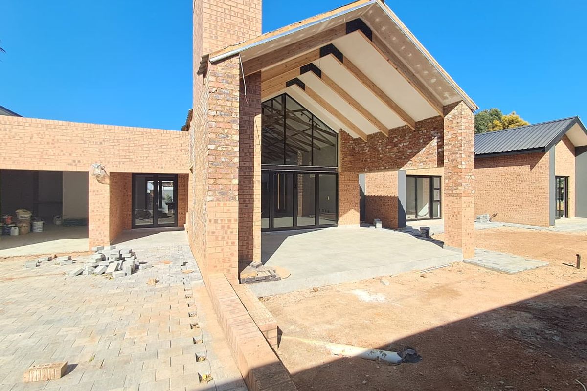Rear view of a modern brick house under construction, featuring a covered patio, exposed timber rafters, and large glass doors.