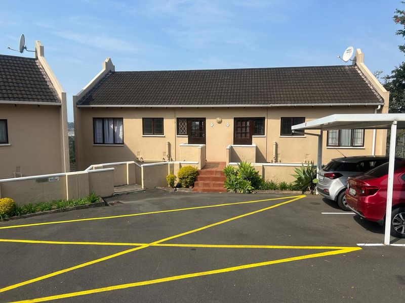 Front elevation of an apartment unit featuring a tiled roof, dedicated carport, and paved driveway access.