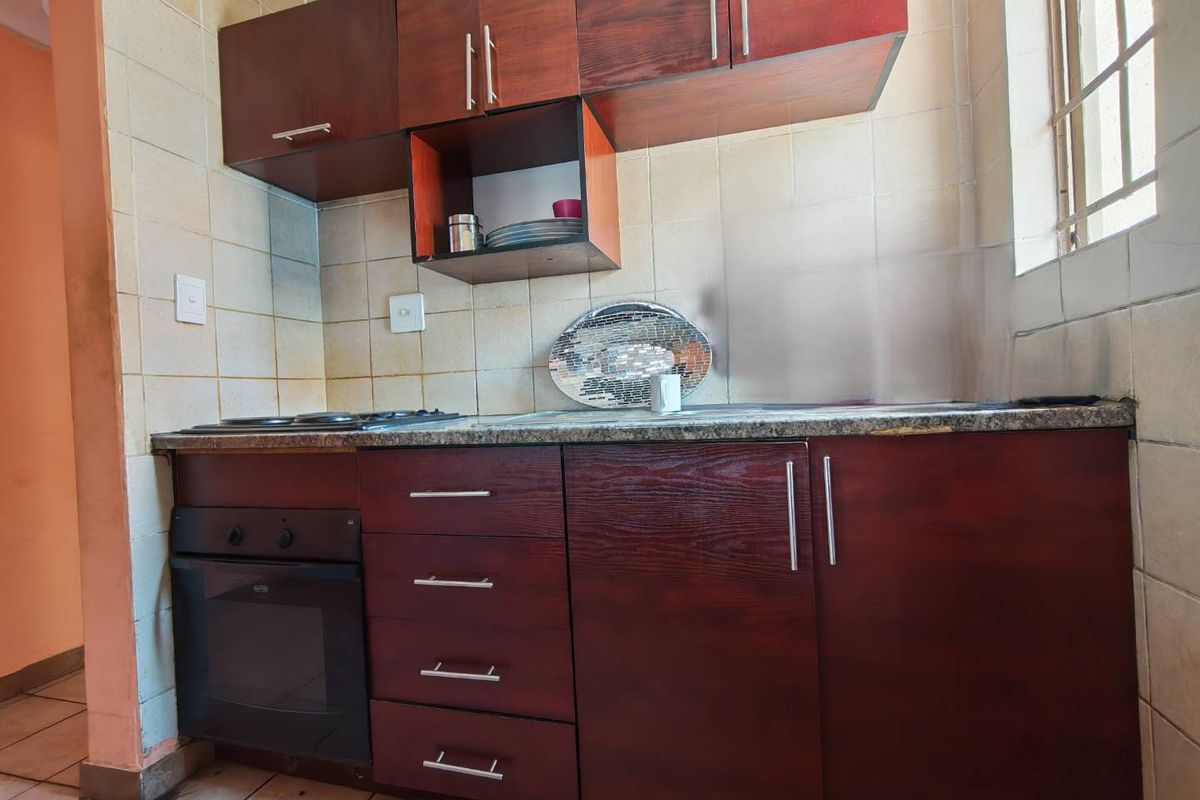 A compact kitchen featuring dark wood cabinetry, a built-in oven, a hob, and tiled wall finishes.