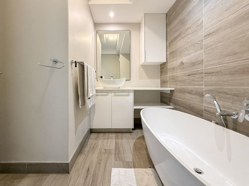 Modern bathroom featuring a sleek freestanding bathtub, vessel sink vanity, and contemporary wood-look tile finishes throughout.