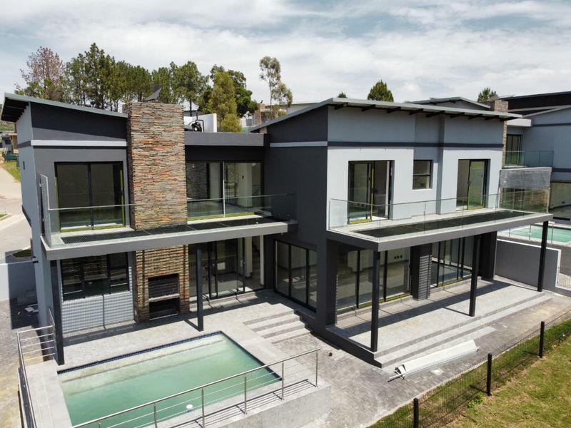 Modern double-story residence featuring a swimming pool, expansive paved patio, stone-clad chimney, and upper-level balconies with glass balustrades.