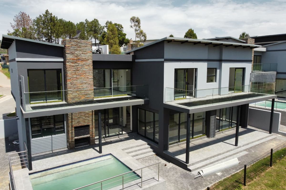 Modern double-story residence featuring a swimming pool, expansive paved patio, stone-clad chimney, and upper-level balconies with glass balustrades.