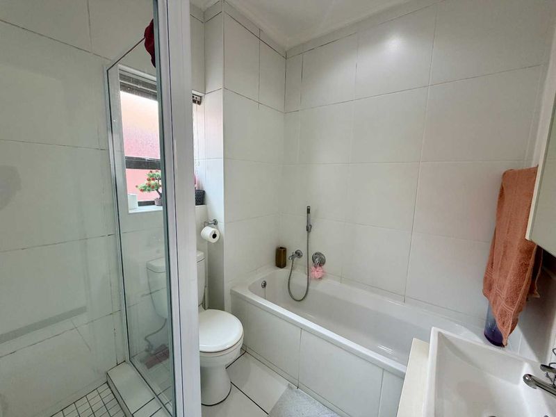 A functional bathroom featuring a shower enclosure, bathtub, toilet, and vanity basin with white wall tiling throughout.
