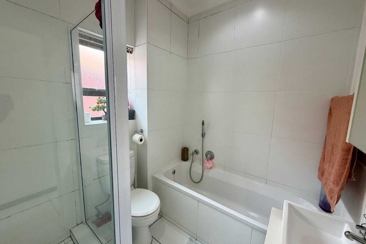 A functional bathroom featuring a shower enclosure, bathtub, toilet, and vanity basin with white wall tiling throughout.
