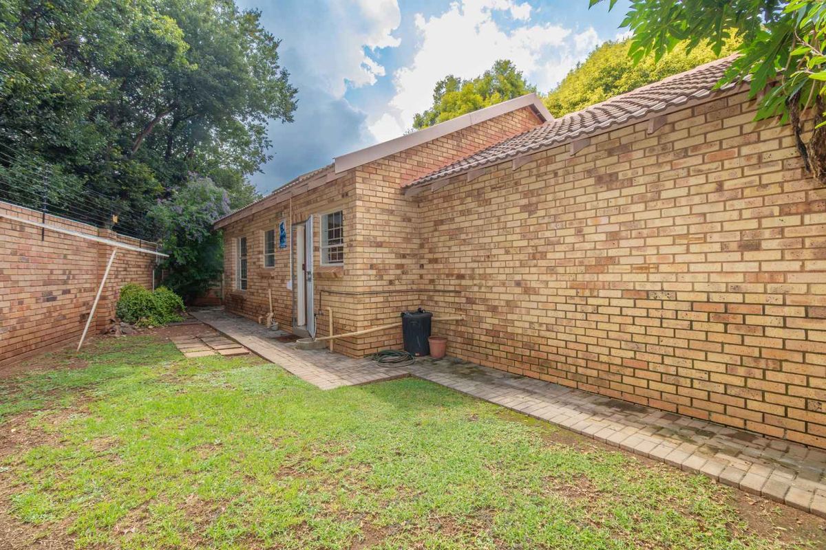 Rear view of the townhouse featuring a face brick exterior, tiled roof, paved walkway, and a private garden area with perimeter electric fencing.