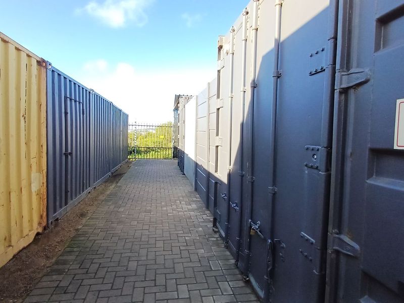 A paved walkway situated between industrial shipping containers, providing access within the property grounds.
