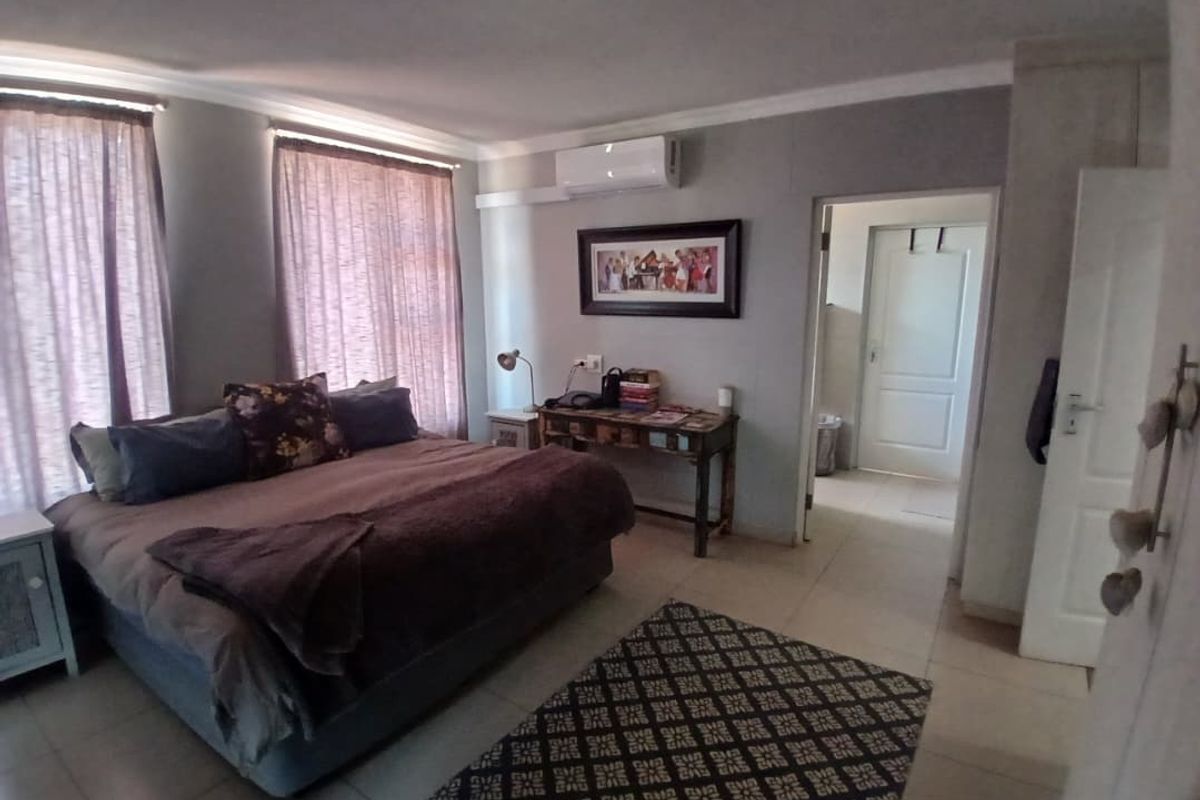 A spacious bedroom featuring tiled flooring, a wall-mounted air conditioning unit, and an adjoining doorway leading to an en-suite or hallway area.