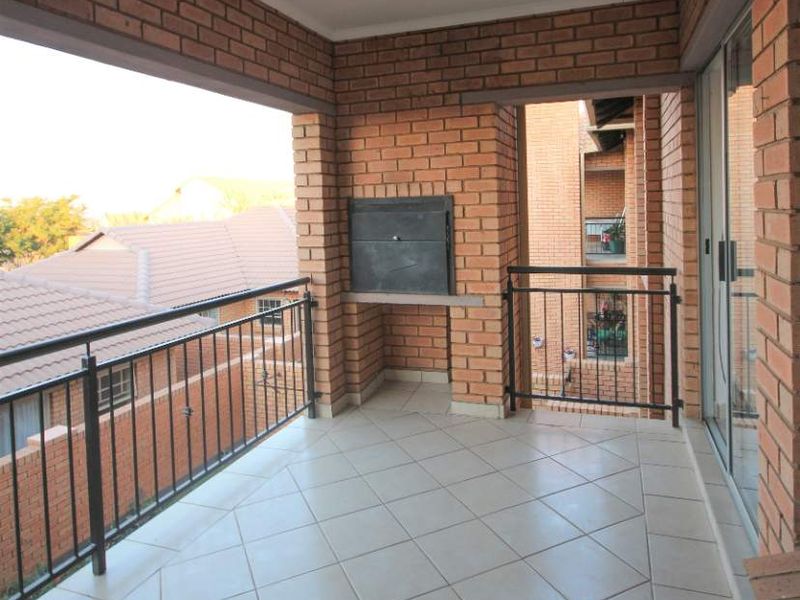A covered balcony featuring tiled flooring, exposed brick walls, and a built-in braai, offering an ideal space for outdoor entertaining.