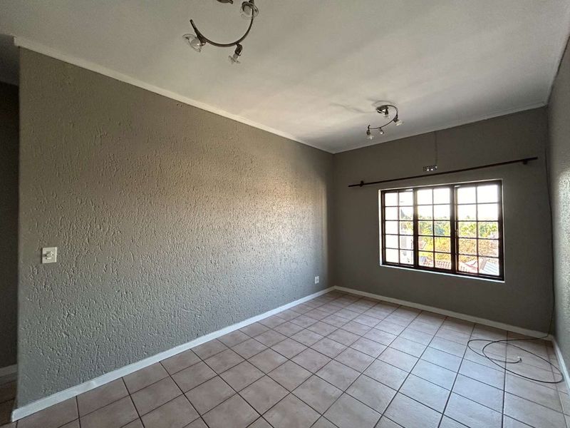 An empty bedroom featuring tiled flooring, textured grey walls, and a multi-pane window providing natural light.