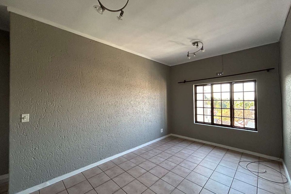 An empty bedroom featuring tiled flooring, textured grey walls, and a multi-pane window providing natural light.