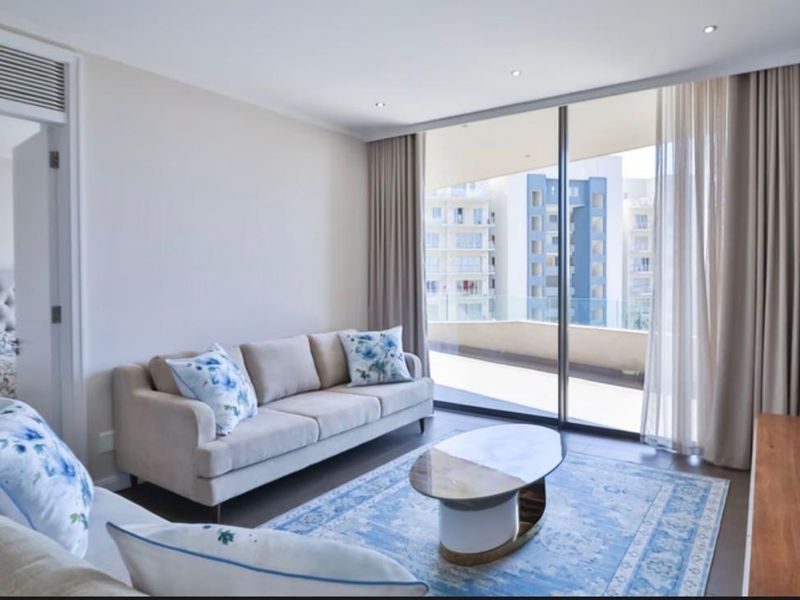 Bright living room featuring large sliding glass doors leading to a balcony, recessed lighting, and neutral finishes, with an adjacent bedroom visible.