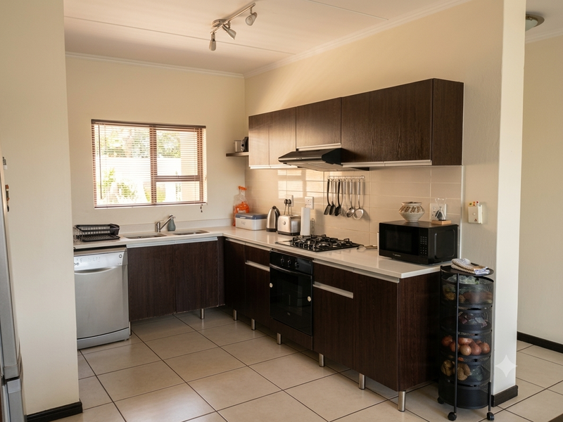 A functional kitchen featuring dark wood cabinetry, white countertops, a gas hob, built-in oven, and tiled flooring with a window for natural light.