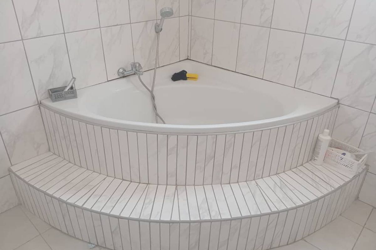 A corner bathtub featuring a raised tiled platform and wall-mounted shower fixture, finished with white marble-effect wall tiles.