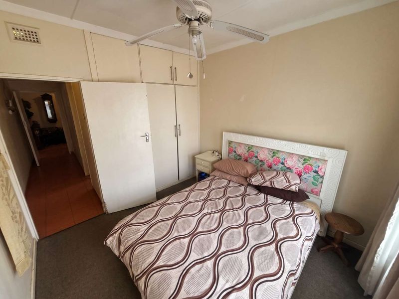 A bedroom featuring built-in cupboards, a ceiling fan, and neutral wall finishes, offering a functional space with potential for cosmetic updates.