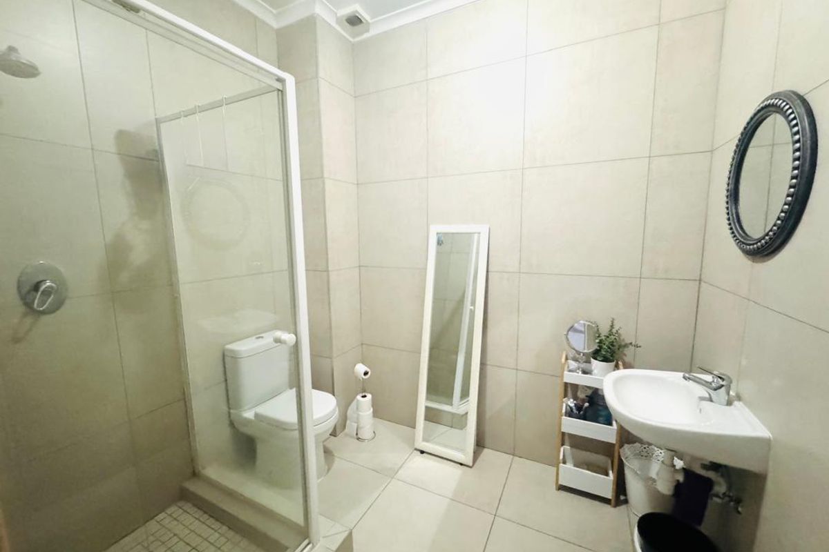A modern bathroom featuring floor-to-ceiling neutral tiling, a glass-enclosed shower, a pedestal basin, and a toilet.
