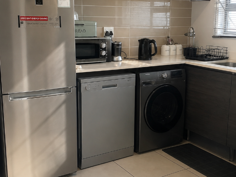 A functional kitchen featuring dark wood cabinetry, a tiled backsplash, neutral floor tiles, and integrated appliances including a dishwasher and washing machine.