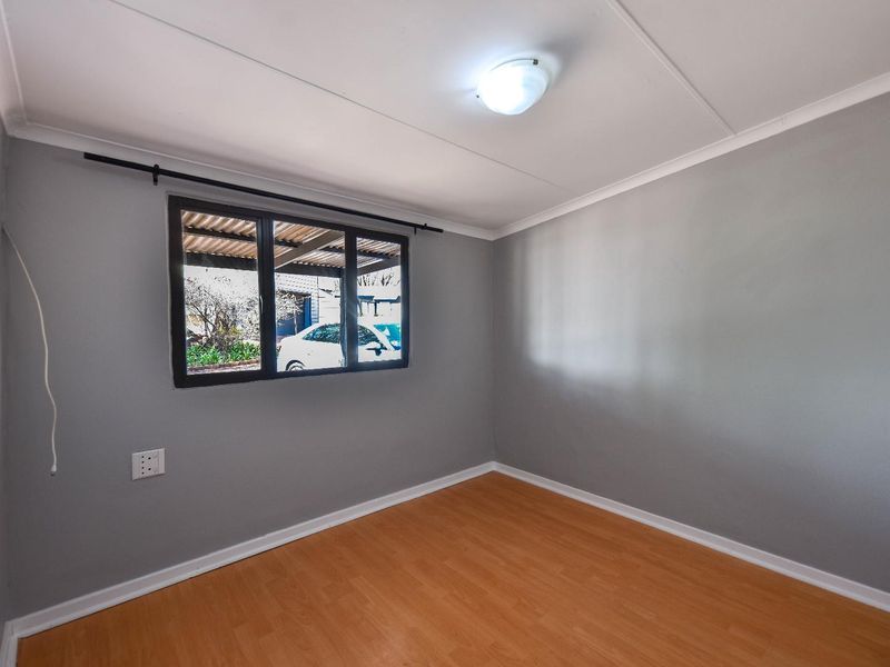 A clean, empty bedroom featuring neutral grey walls, laminate flooring, and a window with a black frame.