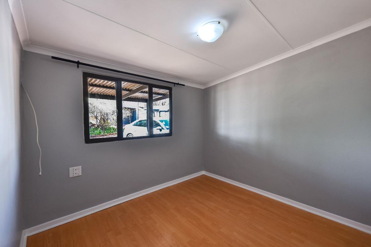 A clean, empty bedroom featuring neutral grey walls, laminate flooring, and a window with a black frame.