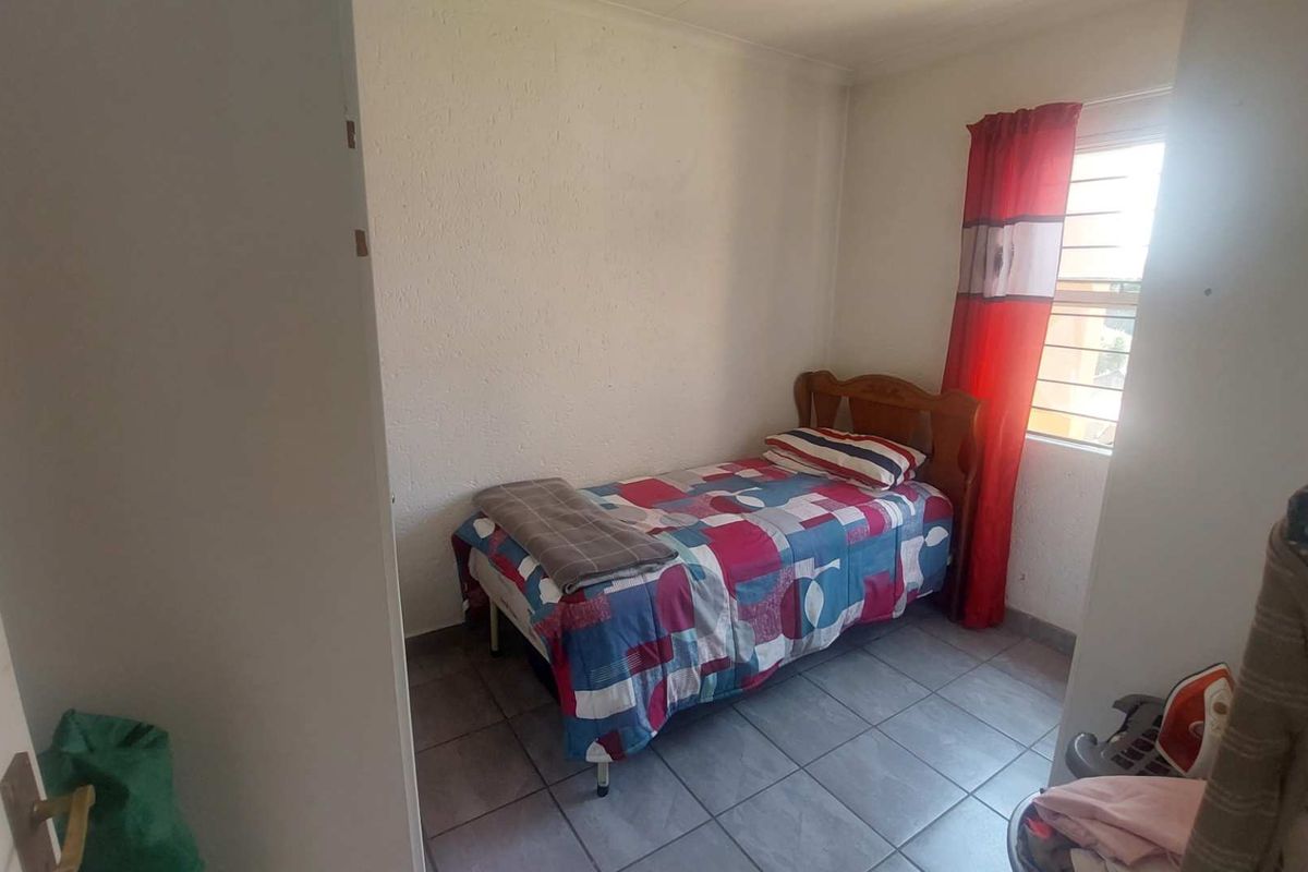 A compact bedroom featuring tiled flooring and a window with security bars, providing a functional living space.
