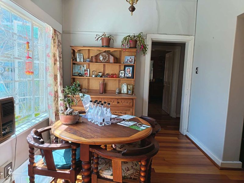 Dining area featuring hardwood flooring, a large window with security bars, and a built-in air conditioning unit, showing signs of wall plaster damage.