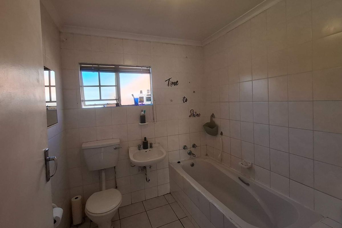 A functional bathroom featuring a bathtub, wall-mounted basin, and toilet, finished with white wall and floor tiles.