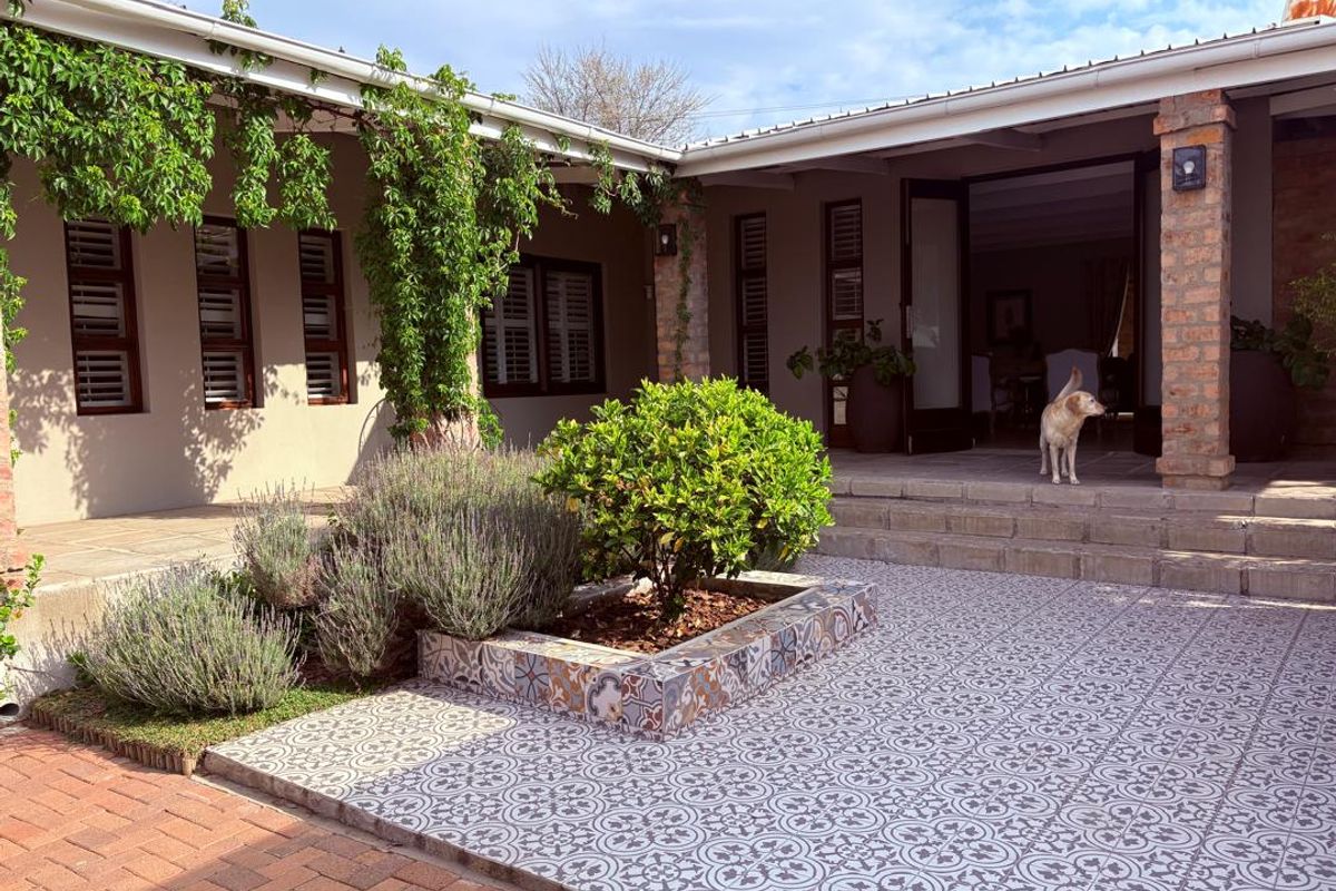 A well-maintained rear patio area featuring decorative patterned tiles, brick pillars, and direct access to the interior through double doors.