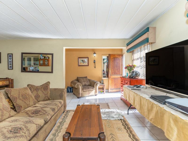 A living room featuring tiled flooring, a timber entrance door, and a panelled ceiling, offering a functional space with potential for cosmetic updates.