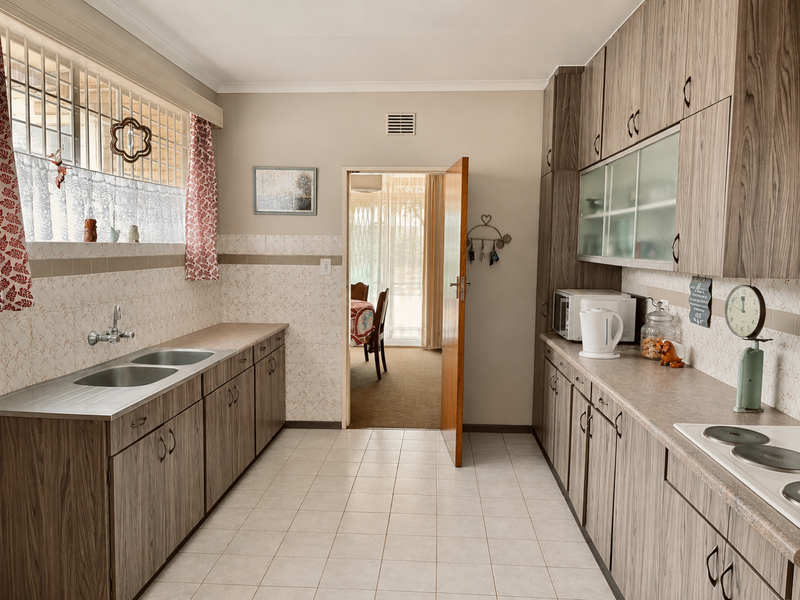 A functional kitchen featuring wood-look laminate cabinetry, a double stainless steel sink, tiled splashbacks, and an integrated electric hob.