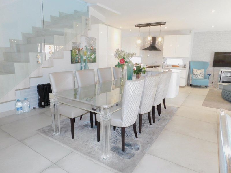 Modern open-plan living and dining area featuring a sleek kitchen with island, glass staircase balustrade, and large format floor tiles.