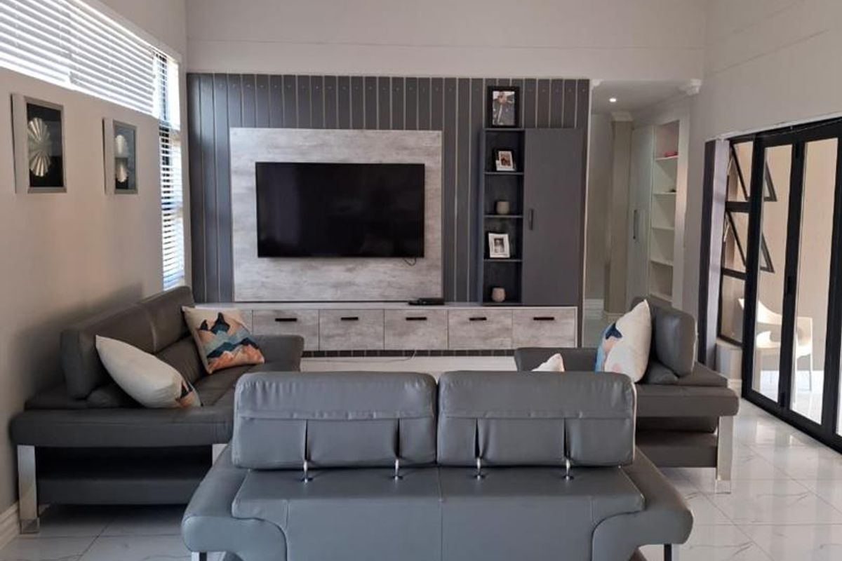 Spacious living room featuring a high vaulted ceiling, modern tiled flooring, and a custom built-in media wall with integrated cabinetry.